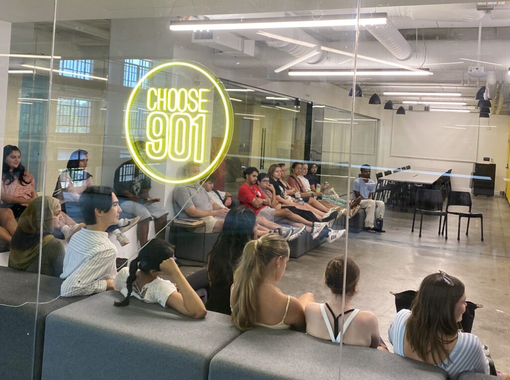 A group of students sit in a room with a Choose 901 sign in the window